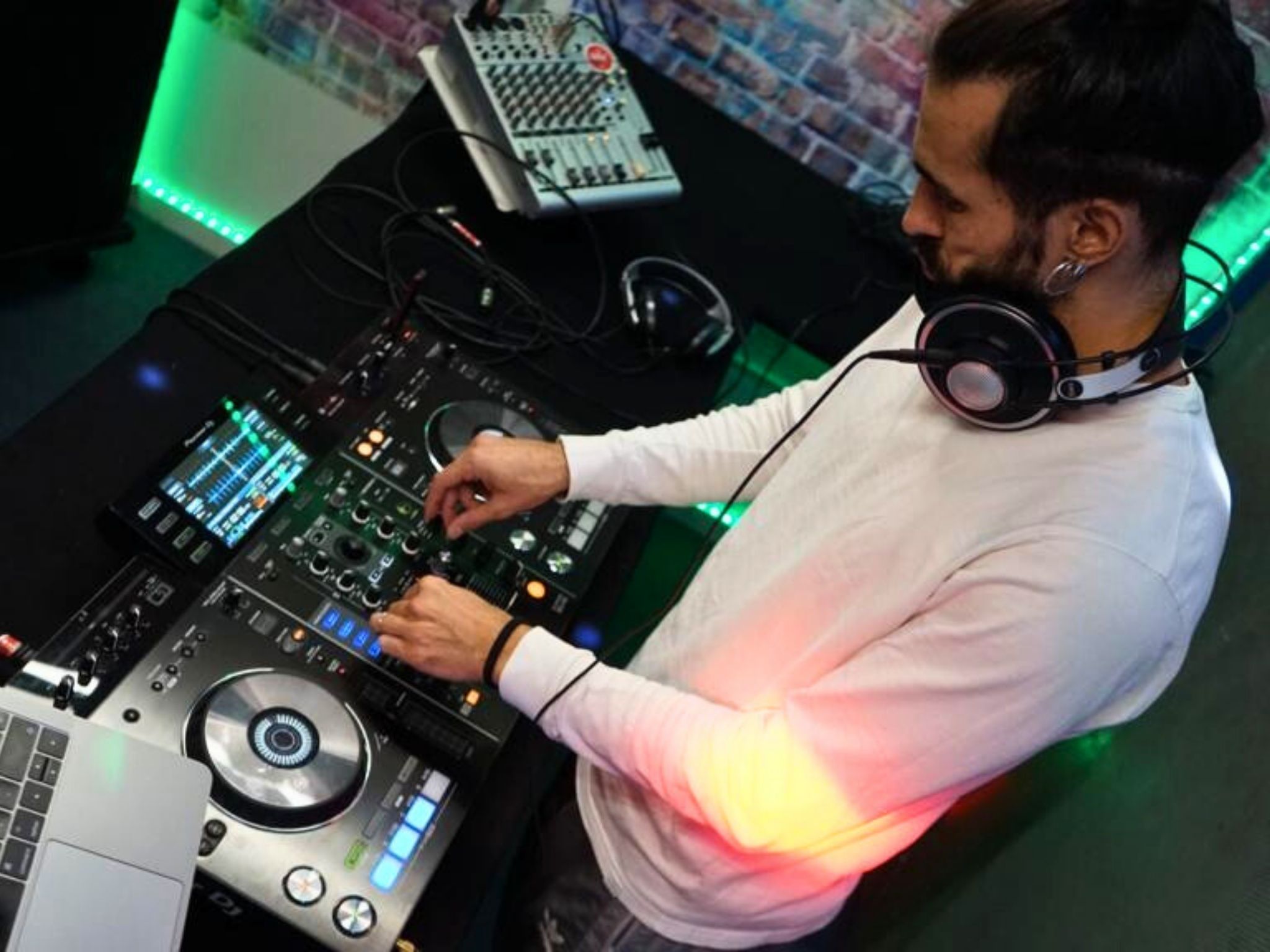 Víctor Óscar Juaranz actuando de DJ y manipulando una consola profesional en una cabina iluminada con luces LED verdes, parte de los servicios de animación musical ofrecidos por OjoArtísticoEvents, dirigida por Víctor Óscar Juaranz.