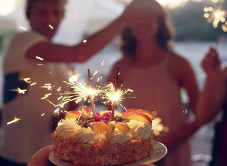Tarta con bengalas encendidas sostenida frente a personas celebrando un cumpleaños.