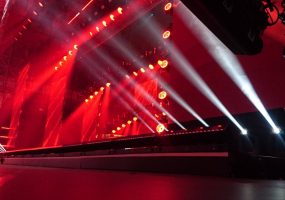 Escenario iluminado con luces rojas y haces de luz blanca, en una producción técnica.