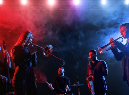 Quinteto de músicos en directo tocando instrumentos de viento, cuerda y percusión, bajo luces teatrales.