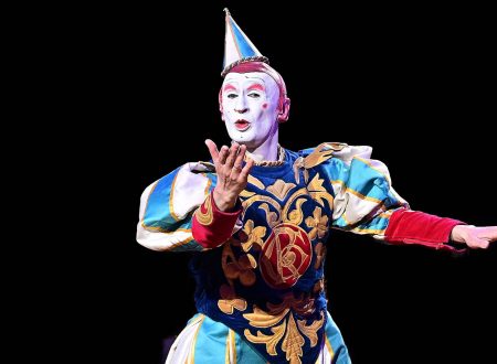 Artista con maquillaje de clown clásico y traje colorido, en plena actuación teatral.