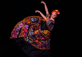 Bailarina con vestido tradicional mexicano bordado, en pleno movimiento durante una actuación artística.