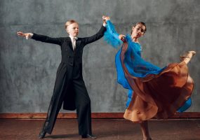 Pareja joven de bailarines en plena pose de danza de salón, con vestimenta formal elegante.