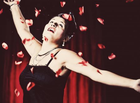 Artista con vestido negro y pétalos rojos en el aire durante un espectáculo.