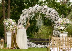 Decoración floral en arco circular para ceremonia al aire libre, con candelabro colgante y disposición elegante.