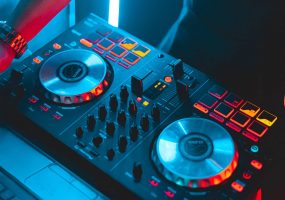 Controladora DJ iluminada en tonos azules y rojos, con una mano ajustando el equipo.