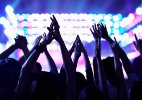 Público en un concierto nocturno con pulseras luminosas verdes, bajo luces azules intensas.