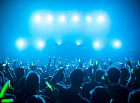 Público en un concierto nocturno con pulseras luminosas verdes, bajo luces azules intensas.