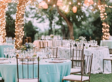 Mesas decoradas al aire libre con luces cálidas y mantelería pastel, en una boda.