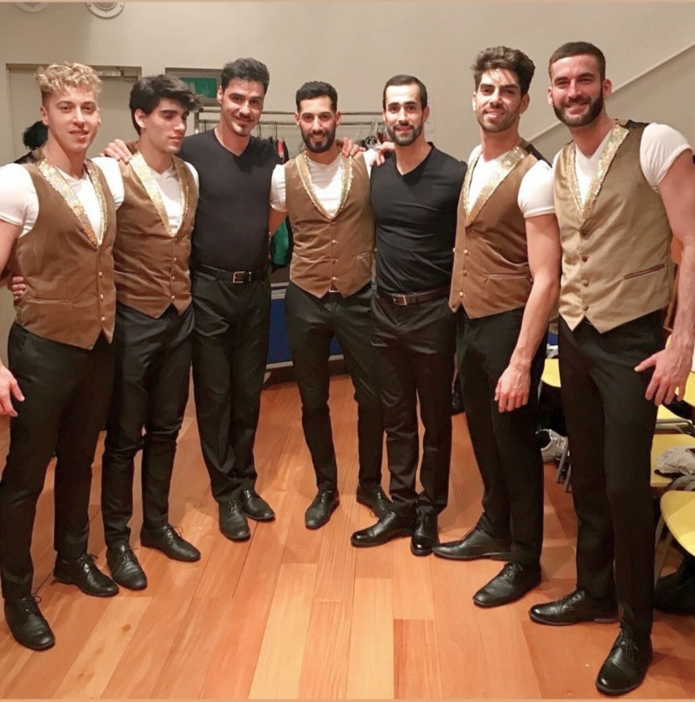 Víctor Óscar Juaranz, responsable de OjoArtísticoEvents, aparece en el centro de la imagen vestido de negro, rodeado de un grupo de artistas varones con chalecos marrones y detalles dorados, posando juntos en un camerino.